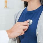 woman-in-navy-shirt-and-grey-cardigan-getting-heart-listened-to-by-doctor