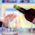 woman-holding-hand-over-stemless-wine-glass-to-stop-pour-of-red-wine