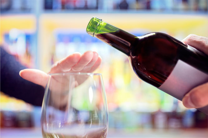 woman-holding-hand-over-stemless-wine-glass-to-stop-pour-of-red-wine