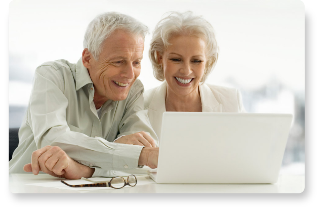 Two elderly people with pal skin smile as they look at something on a laptop