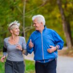 An elderly man and woman smile at each other while they're out for a jog at a park