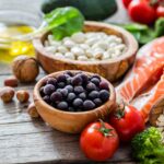 A pile of unprepared food, including raw salmon, blueberries, tomatoes, and hazelnuts