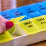 A hand opening the Tuesday morning compartment on a weekly pill organizer