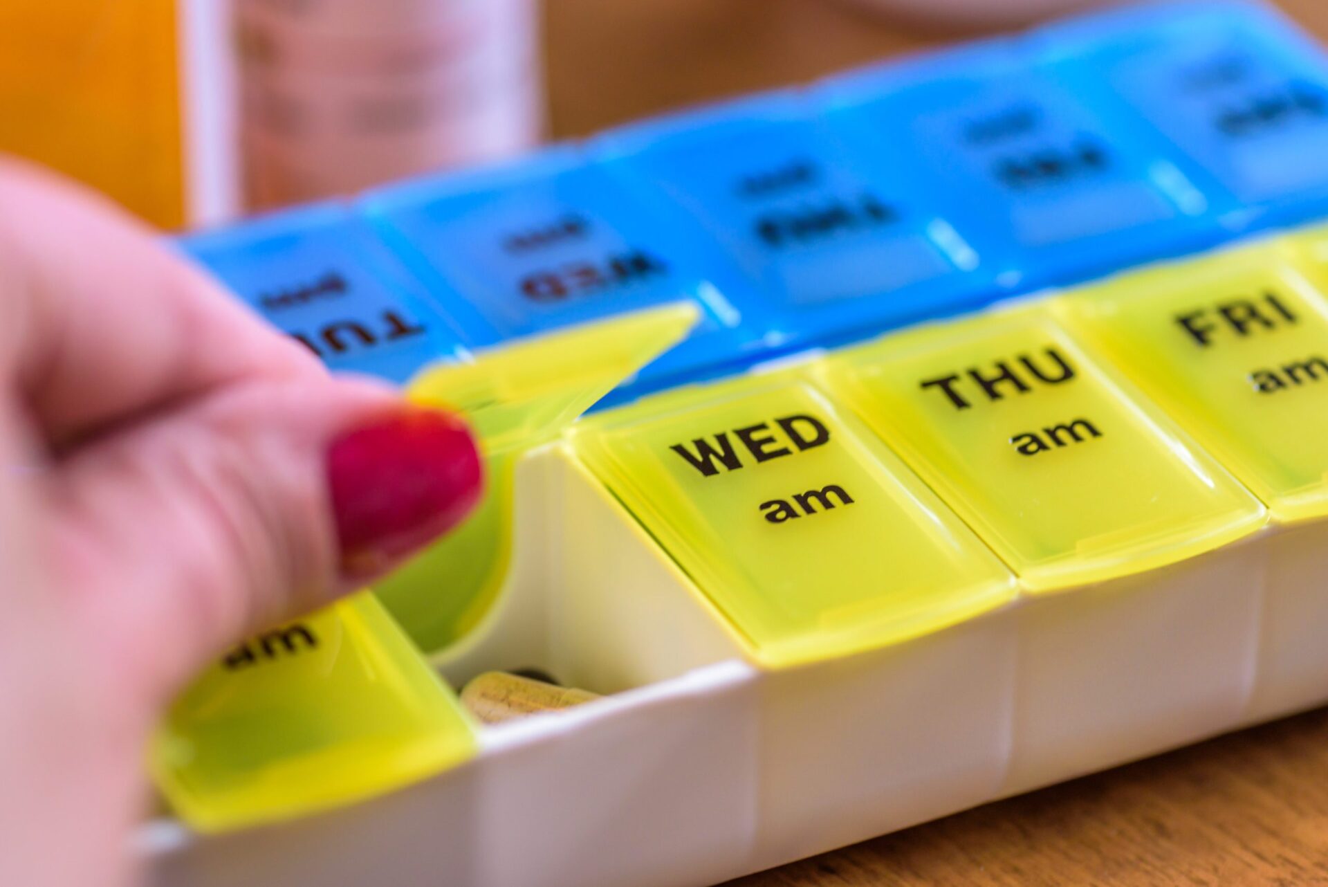 A hand opening the Tuesday morning compartment on a weekly pill organizer