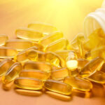 A pile of clear, yellow pills spilling from a pill bottle on a golden orange background
