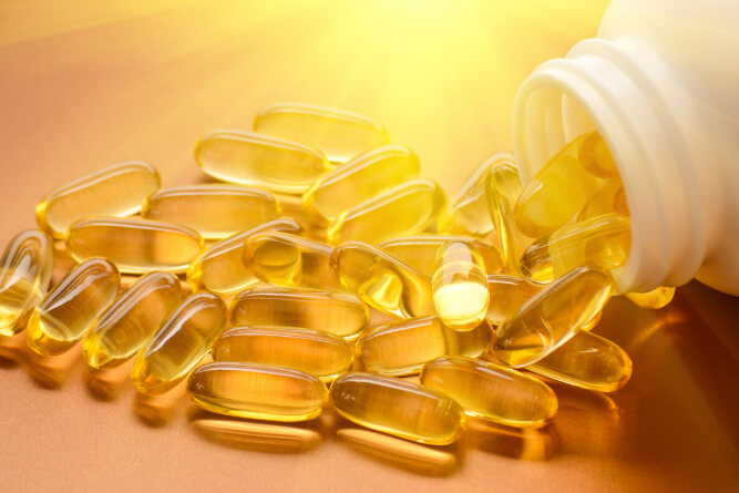 A pile of clear, yellow pills spilling from a pill bottle on a golden orange background