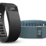 Two Fitbit health monitor wristbands, one black and one teal, on a white background.