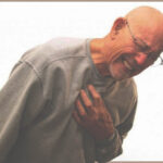 An elderly man looks pained while bending over and clutching his chest